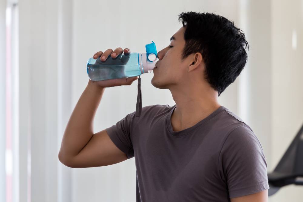 Na zdjęciu widoczny mężczyzna, który pije wodę z elektrolitami, aby pozbyć się kaca. Kadr portretowy. 