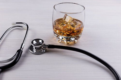 Na zdjęciu widoczna szklanka z whisky i lodem oraz stetoskop. Kadr wąski. 