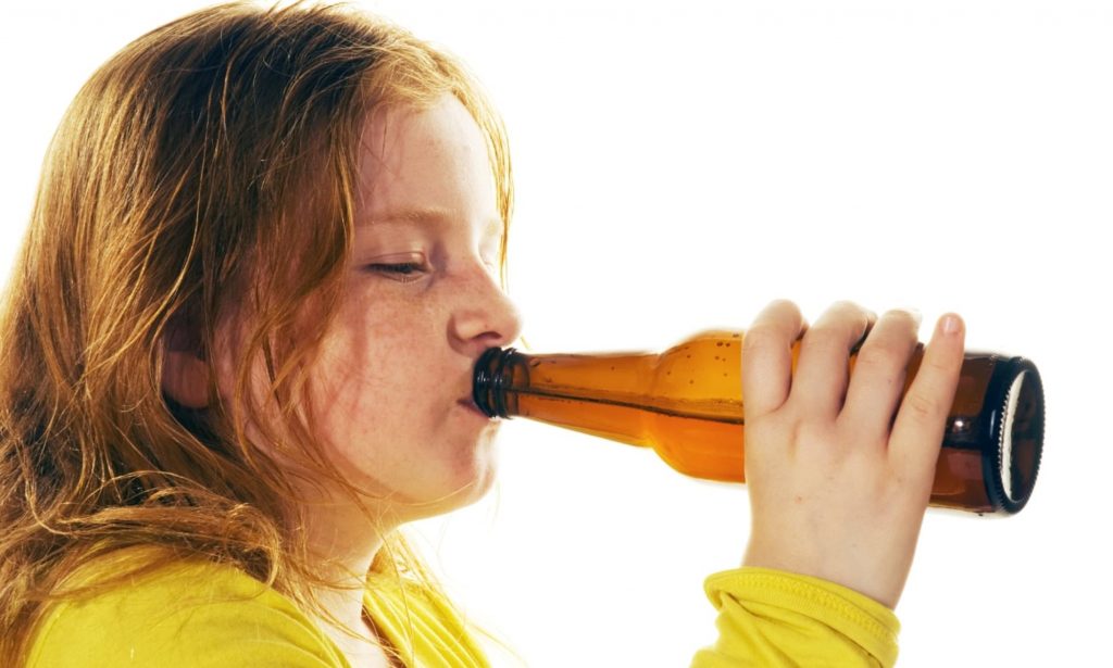 Na zdjęciu widoczna bardzo młoda dziewczynka, która pijemy piwo z butelki. Kadr portretowy. 