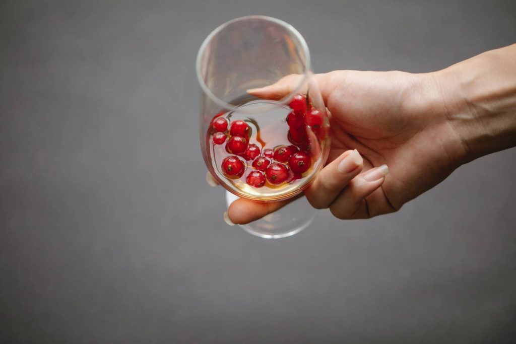 Na zdjęciu widoczna ręka trzymająca kieliszek z alkoholem i owocami. Ujęcie od góry, wąski kadr. 